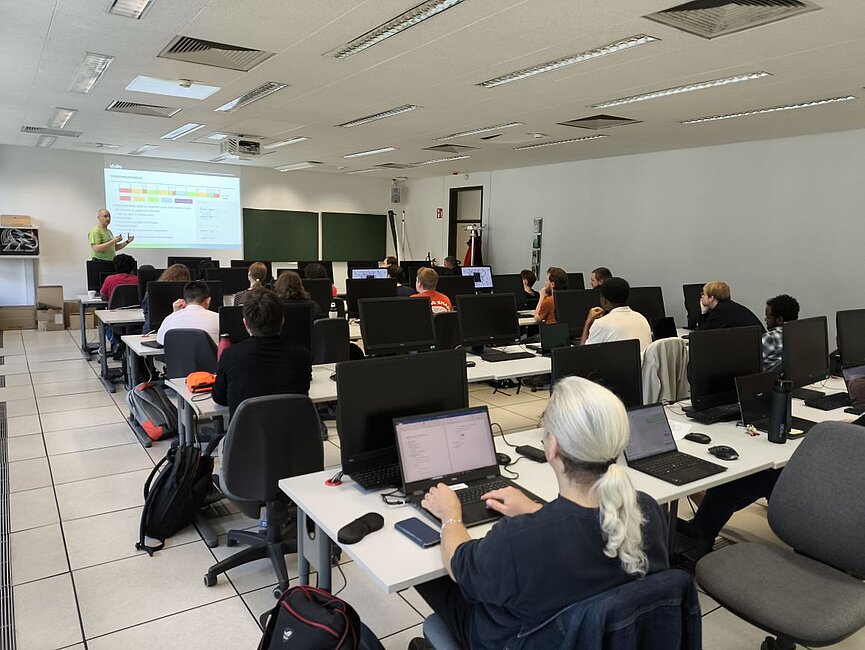 Die Kursteilnehmenden sind vor ihren Laptops sitzend zu sehen, mit Blick auf den Dozenten gerichtet.